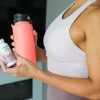 Woman holding Bottle of total gut health prebiotic + probiotic supplement and water bottle.