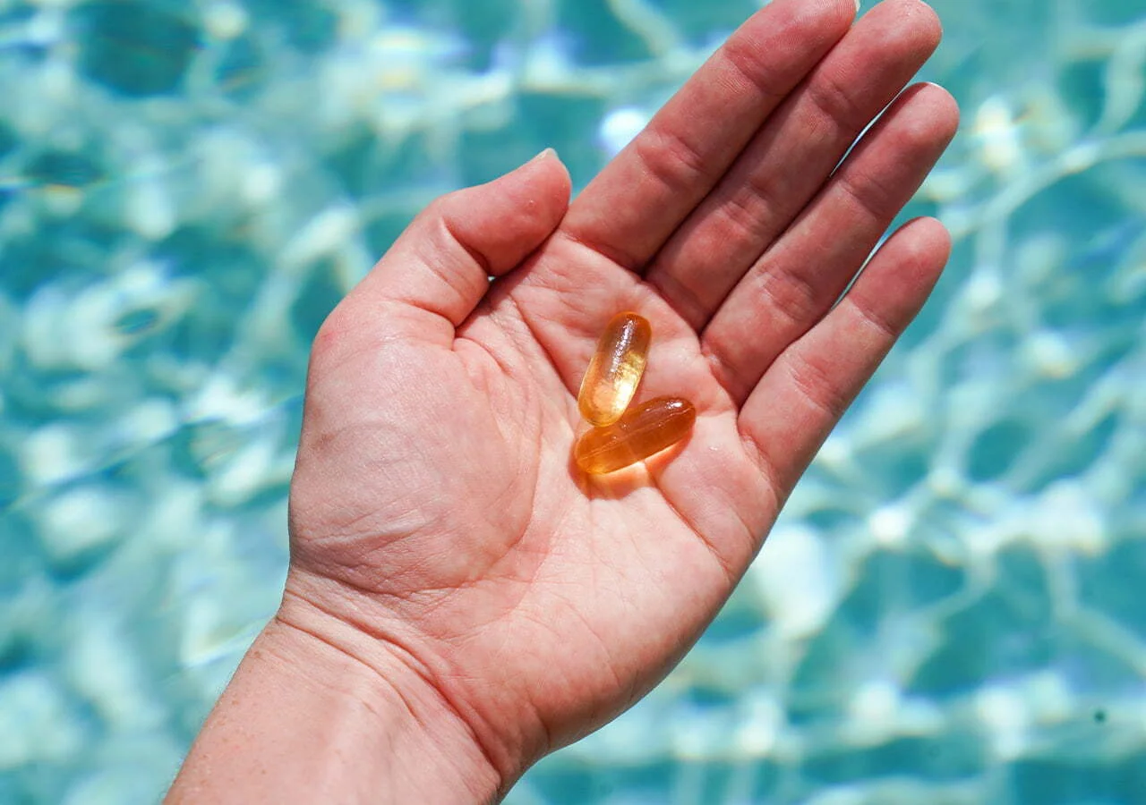 Hand holding two softgels above water.