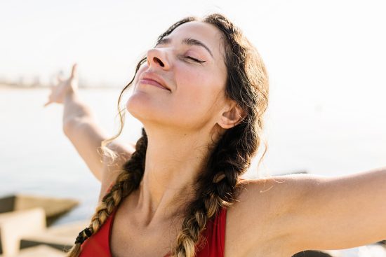 Young woman with closed eyes, a subtle smile, and arms wide open, enjoying the sunshine.