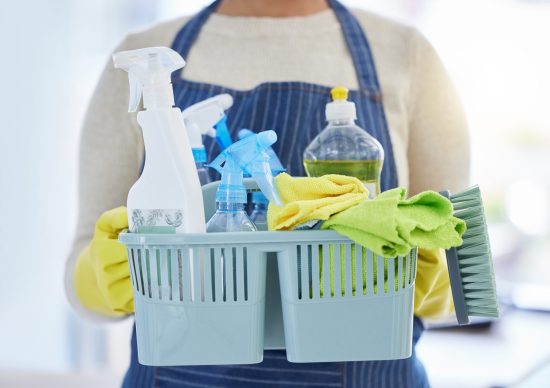 Person holding a plastic basket filled with household cleaning chemicals, an image illustrating the article about detoxing your body.