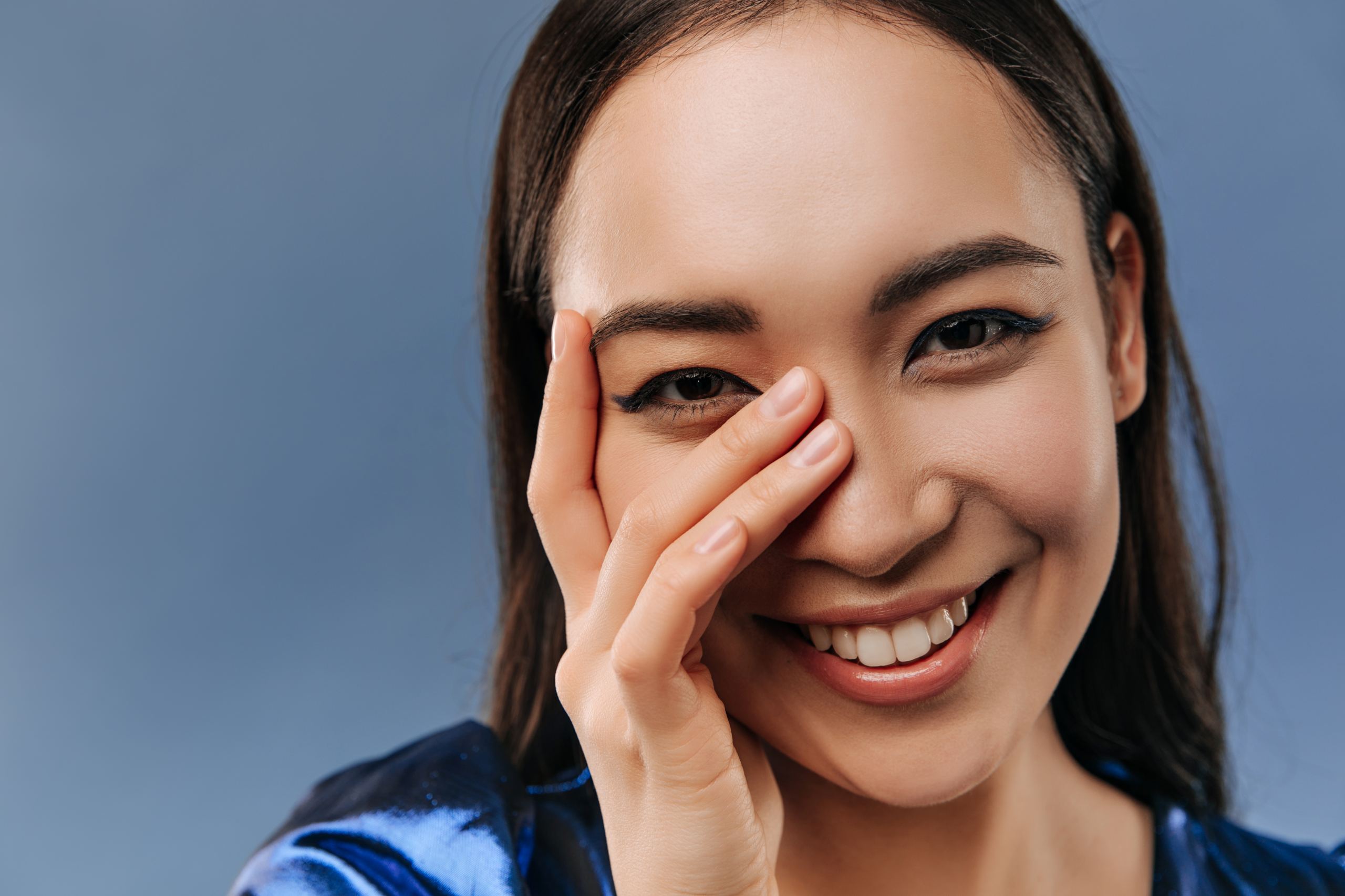A young, smiling woman placing her hand on her face (Eye Health Blog Image).