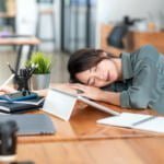 A young woman taking a nap on her desk while at work – a picture illustrating a blog about physical signs of stress.